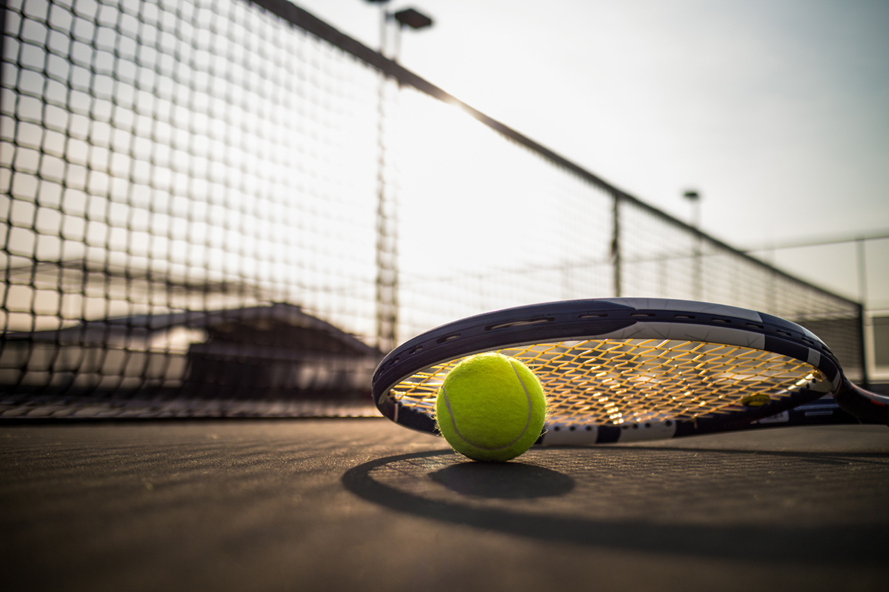 Tennis ball and racket on hard court under sunlight